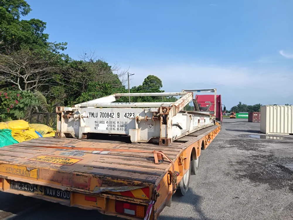 A flat rack loaded on a lowbed trailer in a container yard.